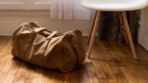 Braune Reisetasche steht auf einem Holzboden